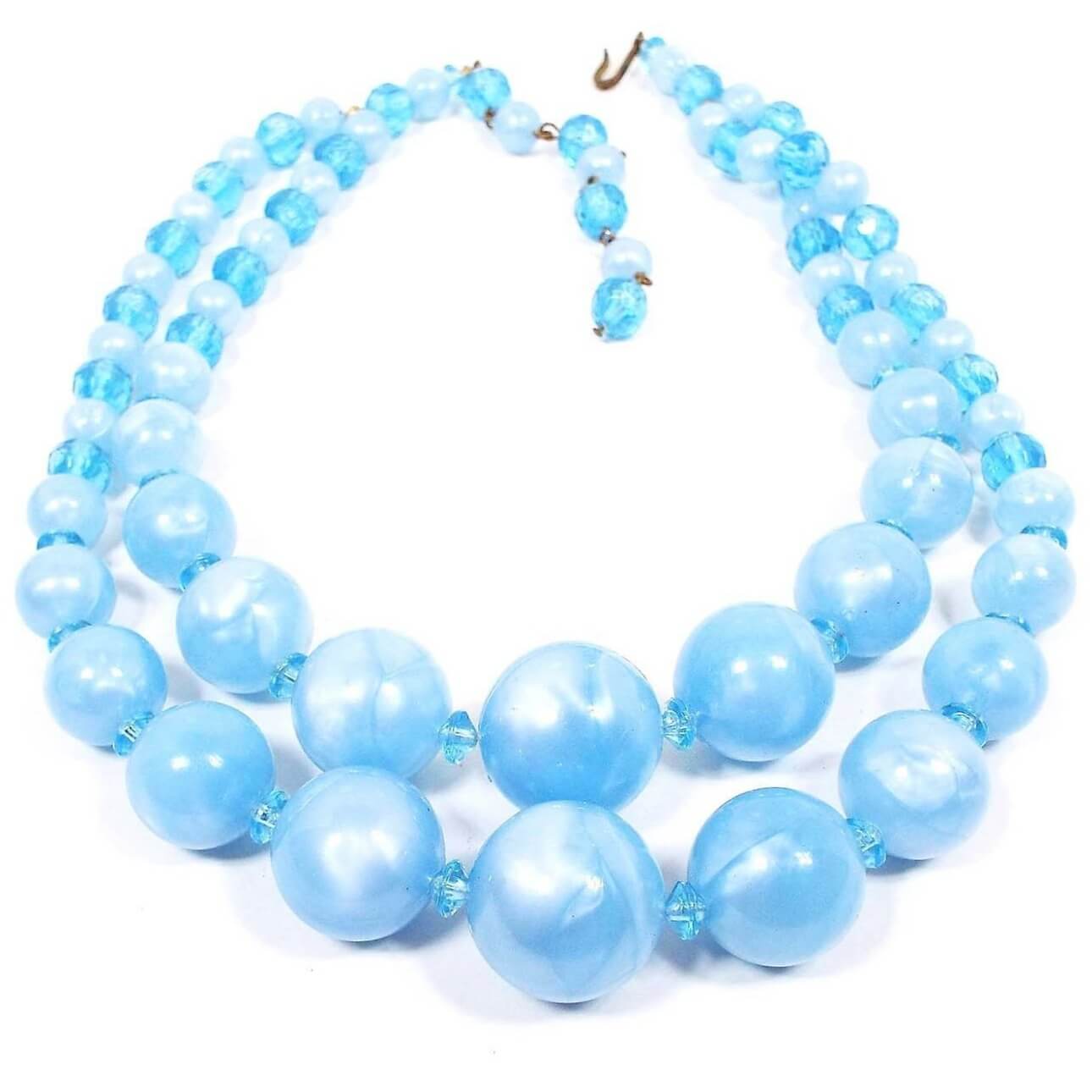 Front view of the Mid Century vintage beaded multi strand necklace. There are round pearly blue lucite beads with translucent blue acrylic disc beads in between them. There are two rows of beads and a hook clasp at the end.