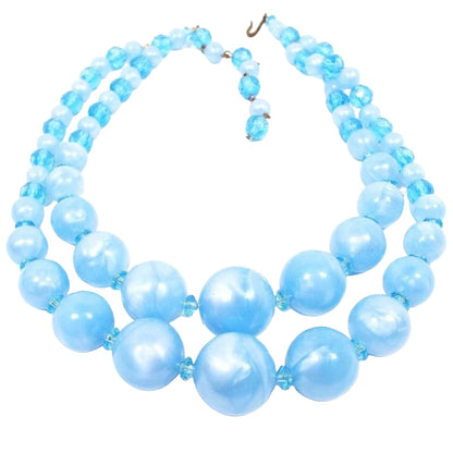 Front view of the Mid Century vintage beaded multi strand necklace. There are round pearly blue lucite beads with translucent blue acrylic disc beads in between them. There are two rows of beads and a hook clasp at the end.