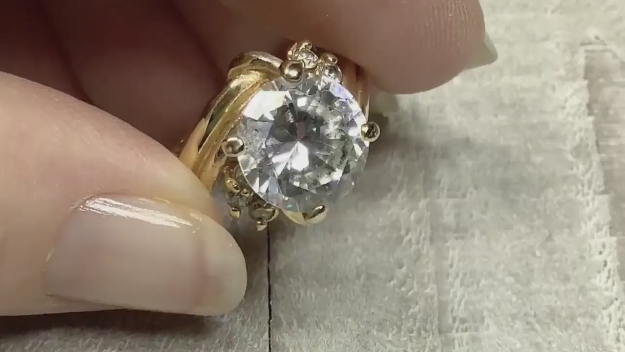 Video of the retro vintage rhinestone cocktail ring. The metal is gold tone in color. There is a large round clear rhinestone at the top and three smaller round clear rhinestones on each side. The video is showing how the rhinestones sparkle.