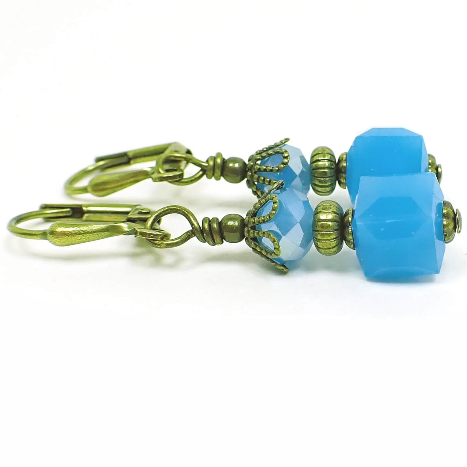 Side view of the small glass beaded earrings. The metal is antiqued brass in color. There are faceted glass crystal rondelle beads at the top and small cube shaped glass beads at the bottom. The beads are mint blue in color.