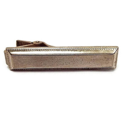 Front view of the Anson Mid Century vintage tie clip. The metal is a darkened gold tone in color from age. It has a rectangle design with a textured beveled edge.