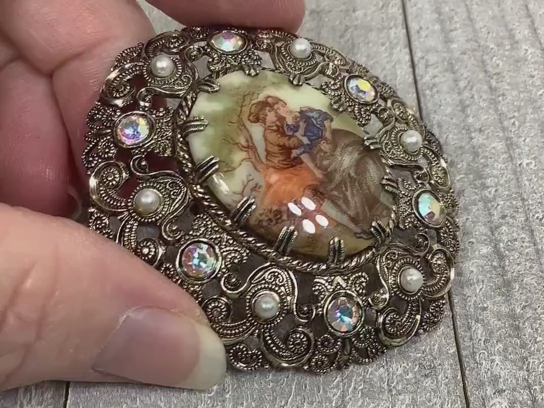 Video showing the Mid Century vintage cameo brooch marked West Germany. It's oval with a cameo of two people in the middle. The outer edge is filigree with faux pearls and AB clear rhinestones. The video shows how the rhinestones sparkle.