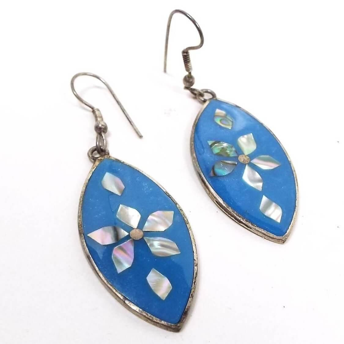 Front view of the retro vintage Southwestern earrings. They are marquis shaped with pearly blue resin and inlaid pieces of abalone shell forming a flower design. The metal is silver tone in color and they have hook style earwires.
