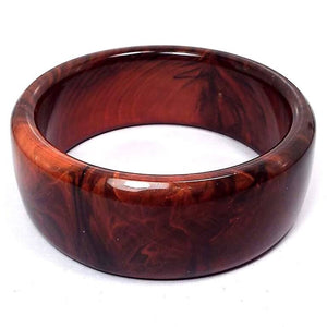 Angled side view of the Mid Century vintage marbled lucite bangle bracelet. It is wide and has marbled shades of brown and orange.