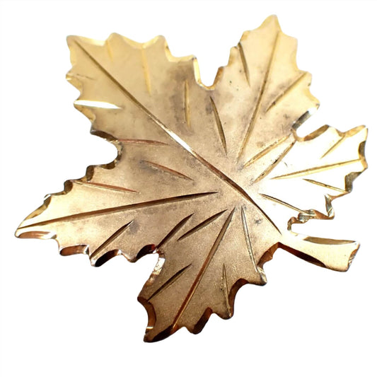 Front view of the vermeil retro vintage Bond Boyd brooch pin. It is shaped like a maple leaf with faceted edges and engraved leaf veins. The metal color is a darkened gold tone as vermeil is a gold plating over sterling silver.