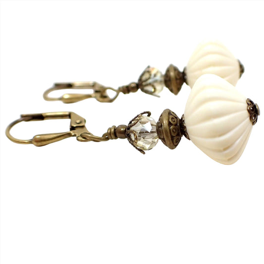 Side view of the handmade vintage lucite drop earrings. The metal is antiqued brass in color. There is an off white cream color vintage lucite corrugated saucer bead at the bottom and a faceted glass crystal at the top. 