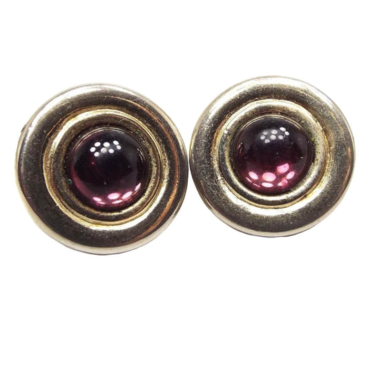Front view of the retro vintage Avon clip on earrings. They are round shaped with gold tone metal. There are purple glass cabs in the middle. 