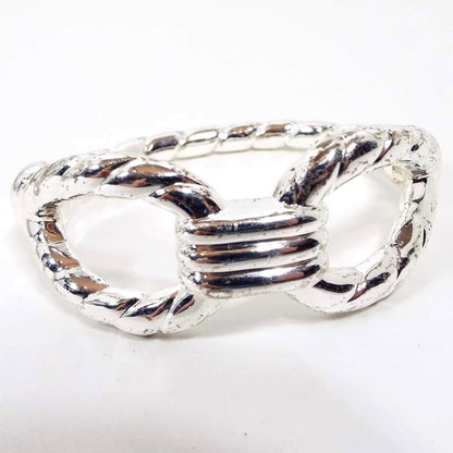 Front view of the retro vintage clamper bracelet, It is silver tone in color with a few tiny spots where it's darkening from age. It has a twisted rope like design that has a large open area on each side. The hinged part of the bracelet is on the side of the bracelet.