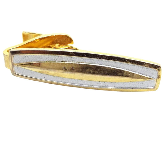 Front view of the retro Modernist style vintage tie clip. It is mostly silver tone in color and has a rounded rectangle shape. The front has matte silver tone with a gold tone stretched oval in the middle.