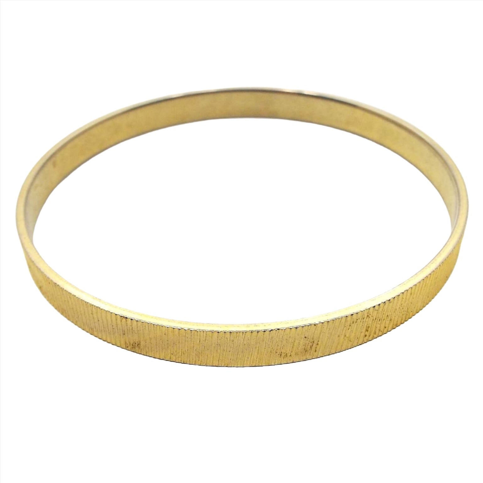 Angled front view of the retro vintage bangle bracelet. It is gold tone in color and is textured with small etched lines all the way around.