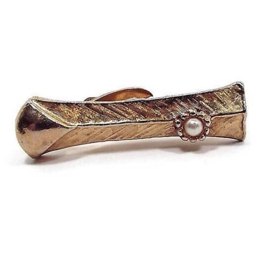 Front view of the Mid Century vintage faux pearl tie clip. The metal is gold tone in color and has a mostly brushed textured design. One end has a small plastic imitation pearl. 