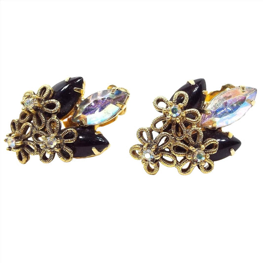 Front view of the Mid Century vintage rhinestone earrings. The metal is gold tone in color and has three flowers at the bottom of each earring. Each flower has an AB rhinestone in the middle. At the top of the earrings are two marquis smooth cab black rhinestones with an AB marquis rhinestone in the middle.
