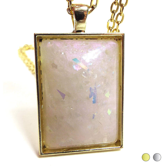 Enlarged view of the large rectangle handmade resin pendant. Pendant is a large rectangle with domed resin cab. The resin is lightly color shift with hues of off white and pink. There is AB glitter embedded in it for some extra sparkle and glitz. In the bottom right corner are color swatches showing a choice of gold tone or silver tone plated setting.