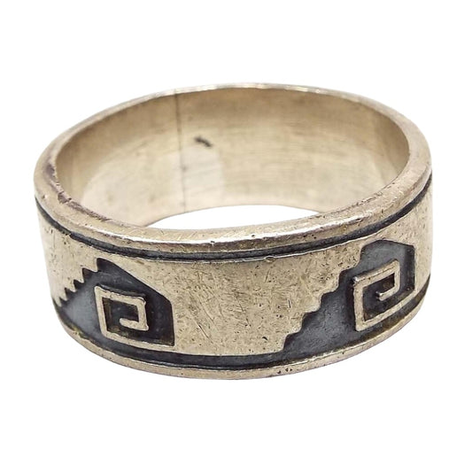 Angled side view of the retro vintage tribal style band ring. The sterling is slightly darkened from age. There is a staircase style design with a square curl in the middle of it. The design is dark gray in color. There is a dark gray line across the top and bottom of the band as part of the design.