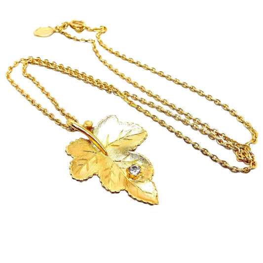 Front view of the retro vintage Avon leaf necklace. The metal is gold tone in color. The pendant is a detailed leaf shape with a single clear round rhinestone towards the bottom.