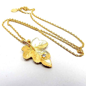 Front view of the retro vintage Avon leaf necklace. The metal is gold tone in color. The pendant is a detailed leaf shape with a single clear round rhinestone towards the bottom.
