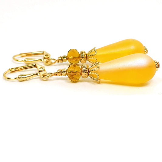 Side view of the handmade teardrop earrings. The metal is gold plated in color. The top beads are small faceted glass dark orange beads and the bottom beads are a frosted rich yellow lucite teardrop bead. 