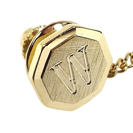 Front view of the Mid Century vintage initial tie tack. It is gold tone in color and has a faceted octagon shape. The front is textured and there is an engraved letter W in the middle.