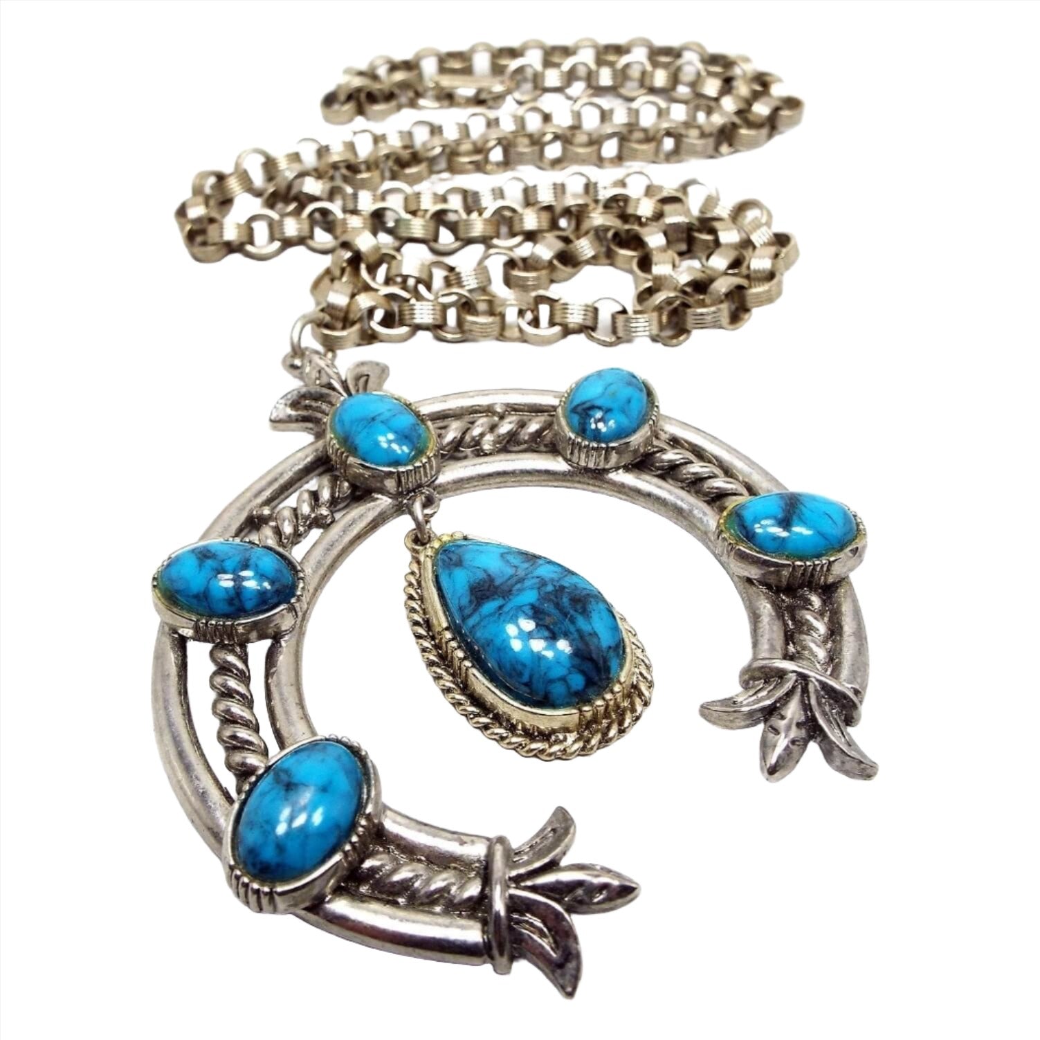 Front view of the retro vintage ART squash blossom pendant necklace. The metal is silver tone in color. The pendant has a large curved squash blossom design with oval blue and gray marbled plastic cabs. 