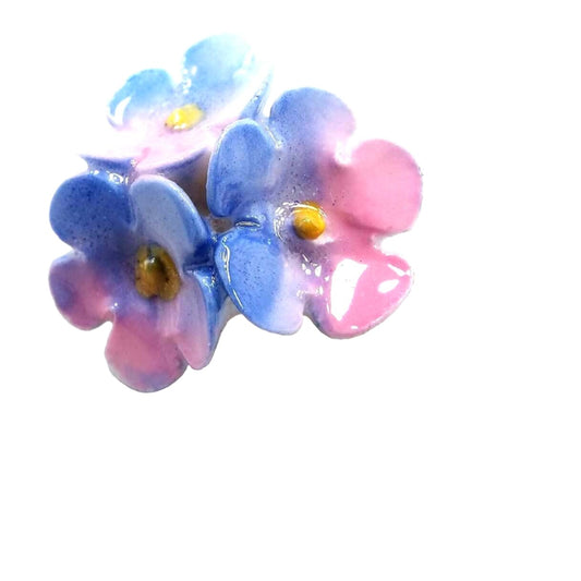 Enlarged view of the top of the porcelain Mid Century floral stick pin. The metal is gold tone in color. There are three porcelain flowers at the top with shades of pink and light blue. 