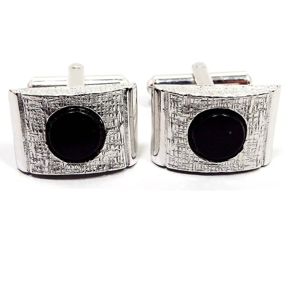 Front view of the retro vintage silver tone and black cufflinks. The have a domed rectangle shape on the front with a flat round black glass cab in the middle. The silver tone metal on the front is textured.