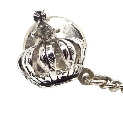 Enlarged view of the Mid Century vintage crown tie tack. It is silver tone in color. The crown has leaves forming the base area, a rhinestone on top of the leaves, and then a cross on the very top.