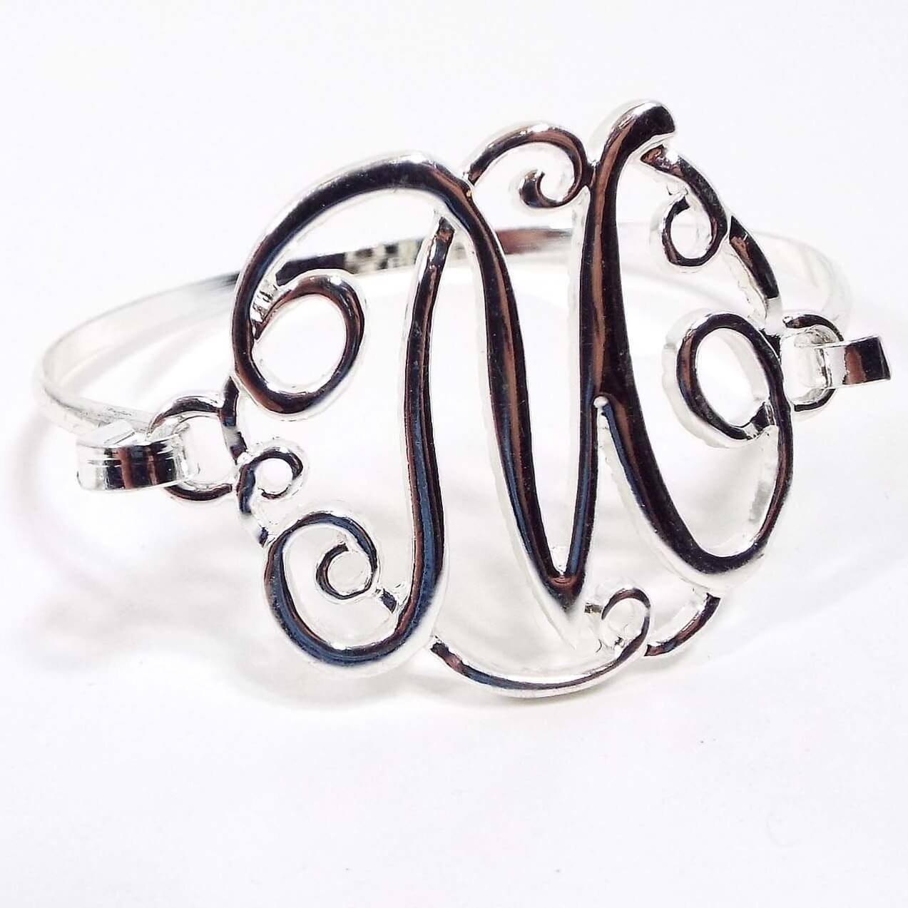 Front view of the retro vintage initial hinged bangle bracelet. The metal is silver tone in color. The top has a large fancy letter M with the clasp the to the bracelet on one side of it.