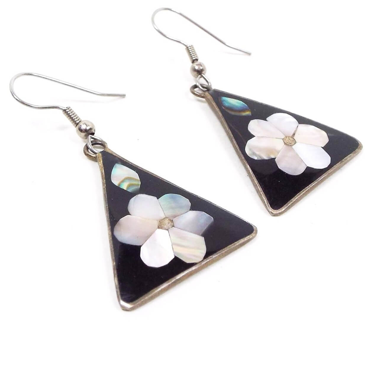 Front view of the retro vintage Southwestern floral earrings. The metal is silver tone in color. There are hook ear wires at the top and triangle drops at the bottom. The triangles are black enameled and have inlaid abalone shell leaves and mother of pearl petals for the flower design.