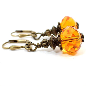 Side view of the handmade short faceted glass crystal drop earrings. The metal is antiqued brass in color. The beads are bright orange in color.
