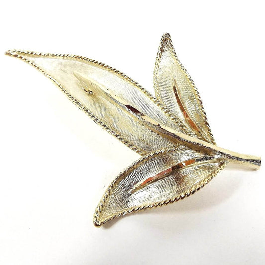 Front view of the retro vintage BSK brooch pin. The metal is textured and a light gold tone in color. It's shaped like a leaf with three leaf areas coming off the stem.