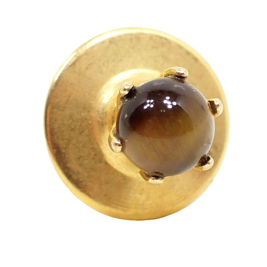 Front view of the Mid Century vintage gemstone stud tie tack. The metal is gold tone in color. There is a small round prong set tiger's eye gemstone on the front that is brown in yellow in color.
