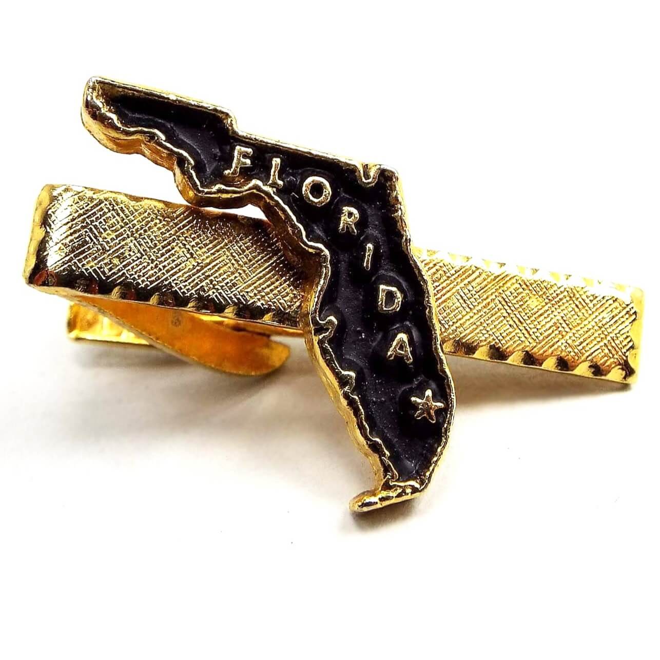 Front view of the retro vintage Florida tie clip. It is textured gold tone color and has a black painted shape of Florida in the middle with the word Florida and a star on it. 
