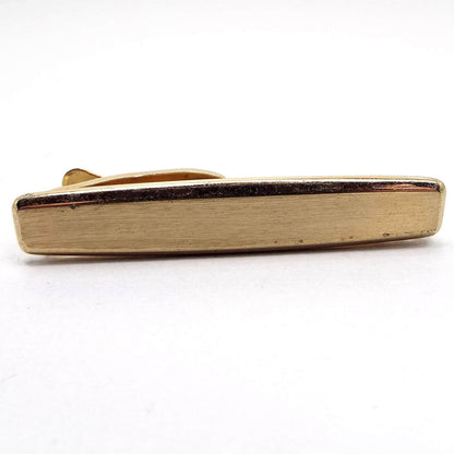 Front view of the Mid Century vintage rounded rectangle tie clip by Hickok. It is gold tone in color and the front has a matte surface. There is a couple of tiny specks of scratching seen from age under magnification.