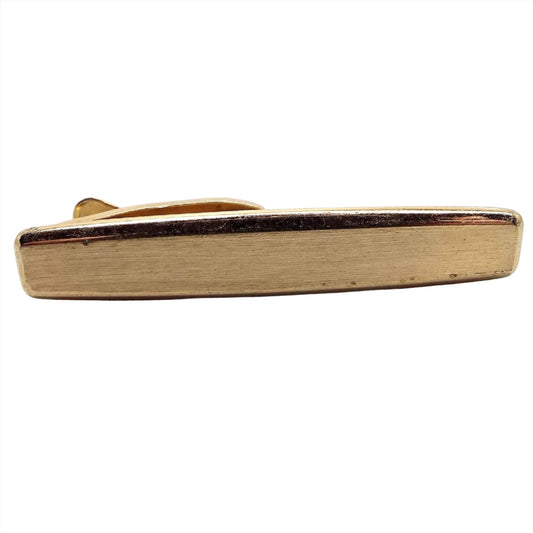 Front view of the Mid Century vintage rounded rectangle tie clip by Hickok. It is gold tone in color and the front has a matte surface. There is a couple of tiny specks of scratching seen from age under magnification.