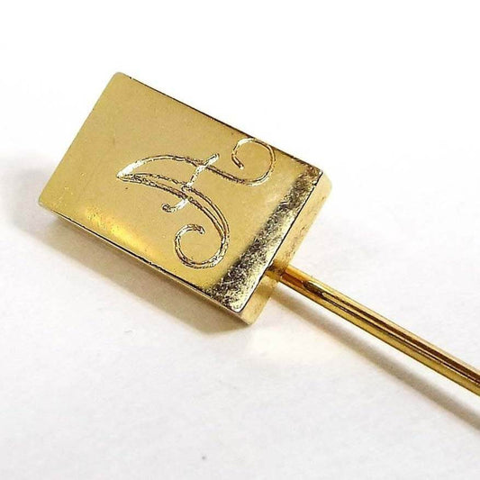 Front view of the Mid Century vintage initial stick pin. The metal is gold tone in color. There is a rectangle at the top with the letter A engraved on it in fancy script.