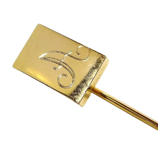 Front view of the Mid Century vintage initial stick pin. The metal is gold tone in color. There is a rectangle at the top with the letter A engraved on it in fancy script.