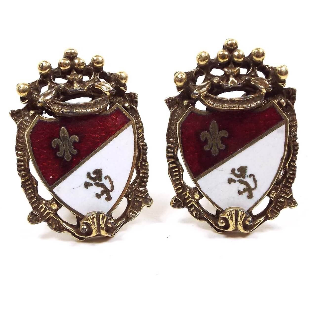 Front view of the Mid Century vintage Coro Heraldic shield clip on earrings. They are antiqued gold tone in color with red and white enamel. There is a fleur de lis and a lion on the front. 