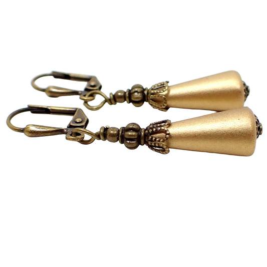 Side view of the handmade cone earrings. The metal is antiqued brass in color. The lucite plastic drops are cone shaped and antiqued gold in color.