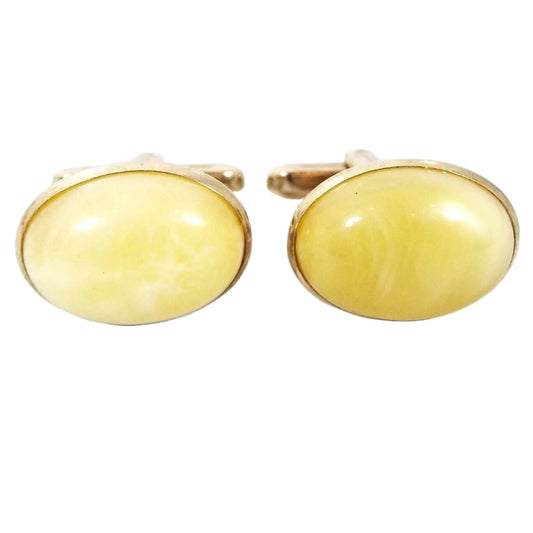 Front view of the Mid Century vintage Hickok lucite cufflinks. They are oval in shape with gold tone color metal. The lucite cabs are domed and a light marbled yellow color.