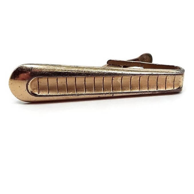 Front view of the Mid Century vintage Foster tie clip. The metal is gold tone in color. it flares out to a rounded end and has line stripes etched down the length of it.