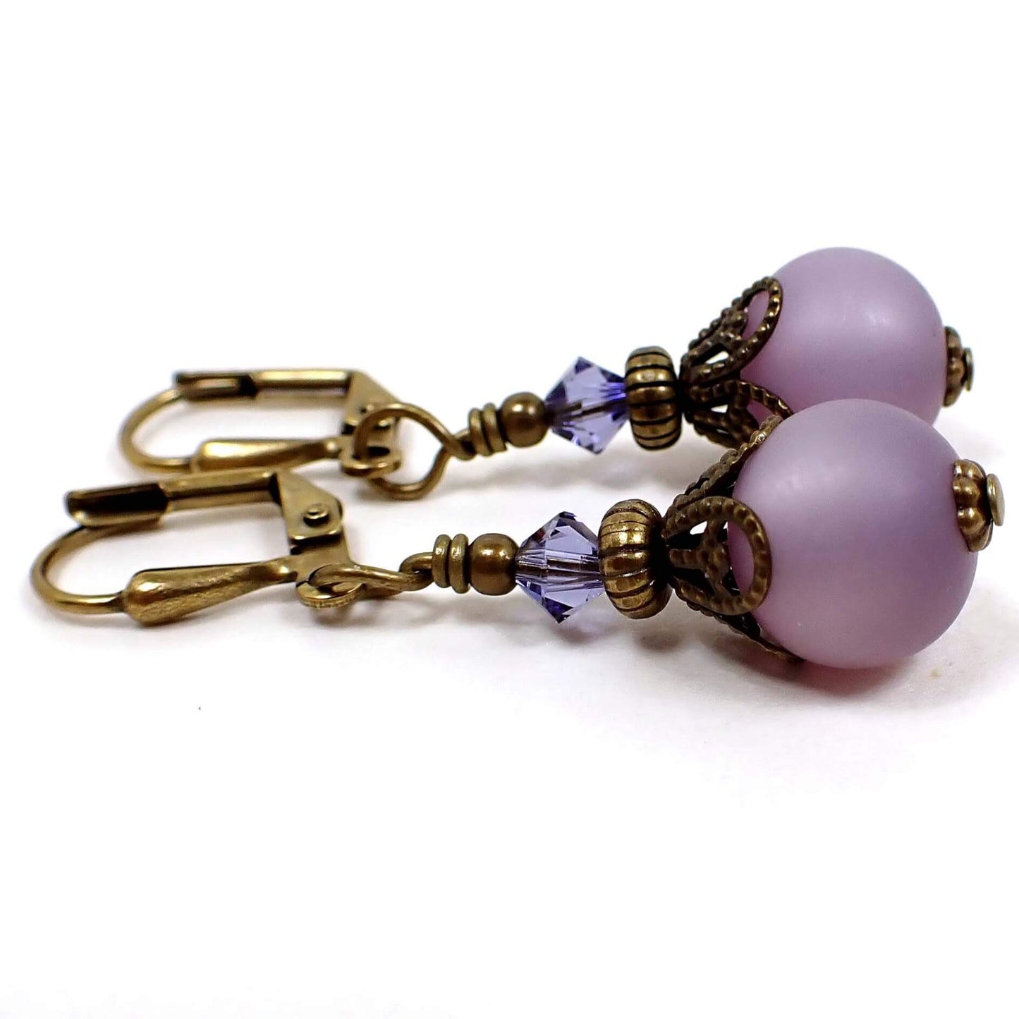 Side view of the small handmade frosted purple lucite drop earrings. The metal in antiqued brass in color. There is a purple glass faceted bead at the top and a round frosted matte purple lucite bead at the bottom.