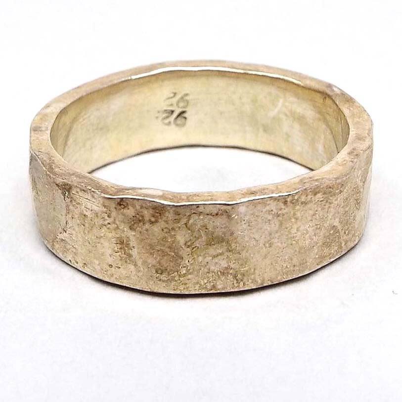Angled side view of the retro vintage sterling silver lightly hammered band ring. The sterling is slightly darkened from age. The outer edge is lightly hammered for an indented textured look. The inside  shows a double stamping of 925. 