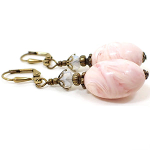 Side view of the handmade earrings with oval vintage lucite beads. The metal is antiqued brass in color. There are faceted glass crystal beads in a semi translucent opal white color on top. The bottom lucite beads have swirled shades of light pink and peach.