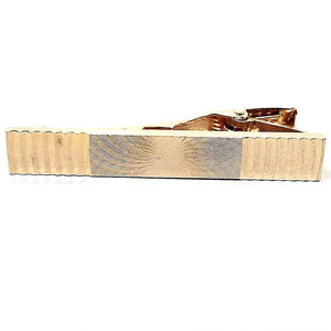 Front view of the retro vintage optical illusion tie clip. It is gold tone in color and has curved lines on each edge. In the middle is a very lightly etched spiral style pattern that gives the optical illusion of movement as you move around in the light.