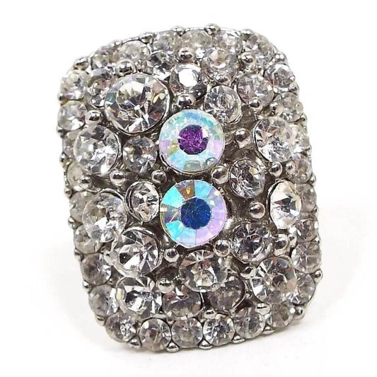 Front view of the retro vintage rhinestone adjustable ring. The metal is silver tone in color. All stones are round shaped and are different sizes. The top of the ring has a large rounded rectangle shape that is slightly curved and is encrusted with clear rhinestones. There are two larger AB rhinestones in the middle area.