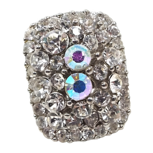 Front view of the retro vintage rhinestone adjustable ring. The metal is silver tone in color. All stones are round shaped and are different sizes. The top of the ring has a large rounded rectangle shape that is slightly curved and is encrusted with clear rhinestones. There are two larger AB rhinestones in the middle area.