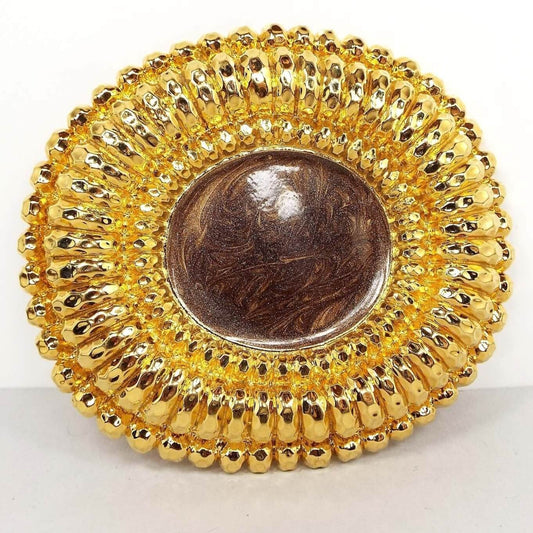 Front view of the retro vintage enameled belt buckle. The metal is gold tone in color. It is oval and has a sunflower like design with the middle having pearly brown marbled enamel. 