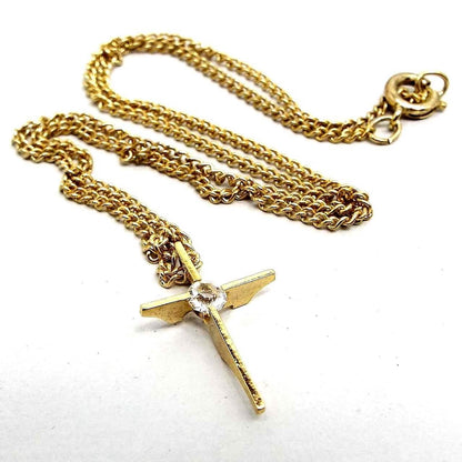 Front view of the retro vintage cross necklace. The metal is gold tone in color. The cross has a plain bar style with curves on the back. There is a single round rhinestone in the middle. Chain has a spring ring clasp on the end.