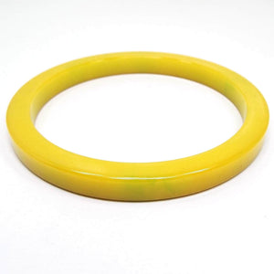Angled view of the Mid Century vintage Bakelite bangle bracelet. The plastic is mostly yellow in color with just a few tiny hints of green here and there. 