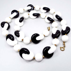 Top view of the retro vintage lucite beaded necklace. The are white round beads all the way down the necklace. In between the white beads are two interlocked beads with one black and one white. There is a spring ring clasp at the end of the necklace.